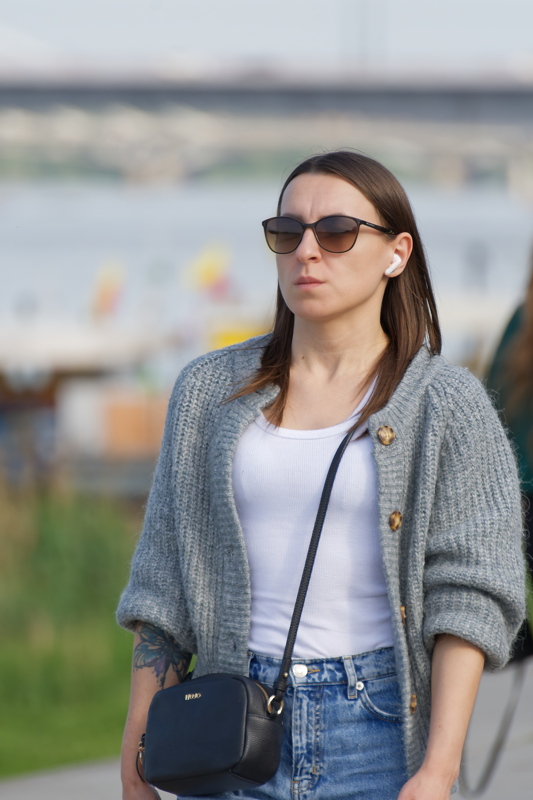 5 - A woman with straight brown hair walking outdoors near a bridge structure